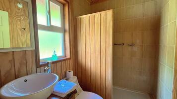 A wooden bathroom with a large window, a white sink, and a shower area.