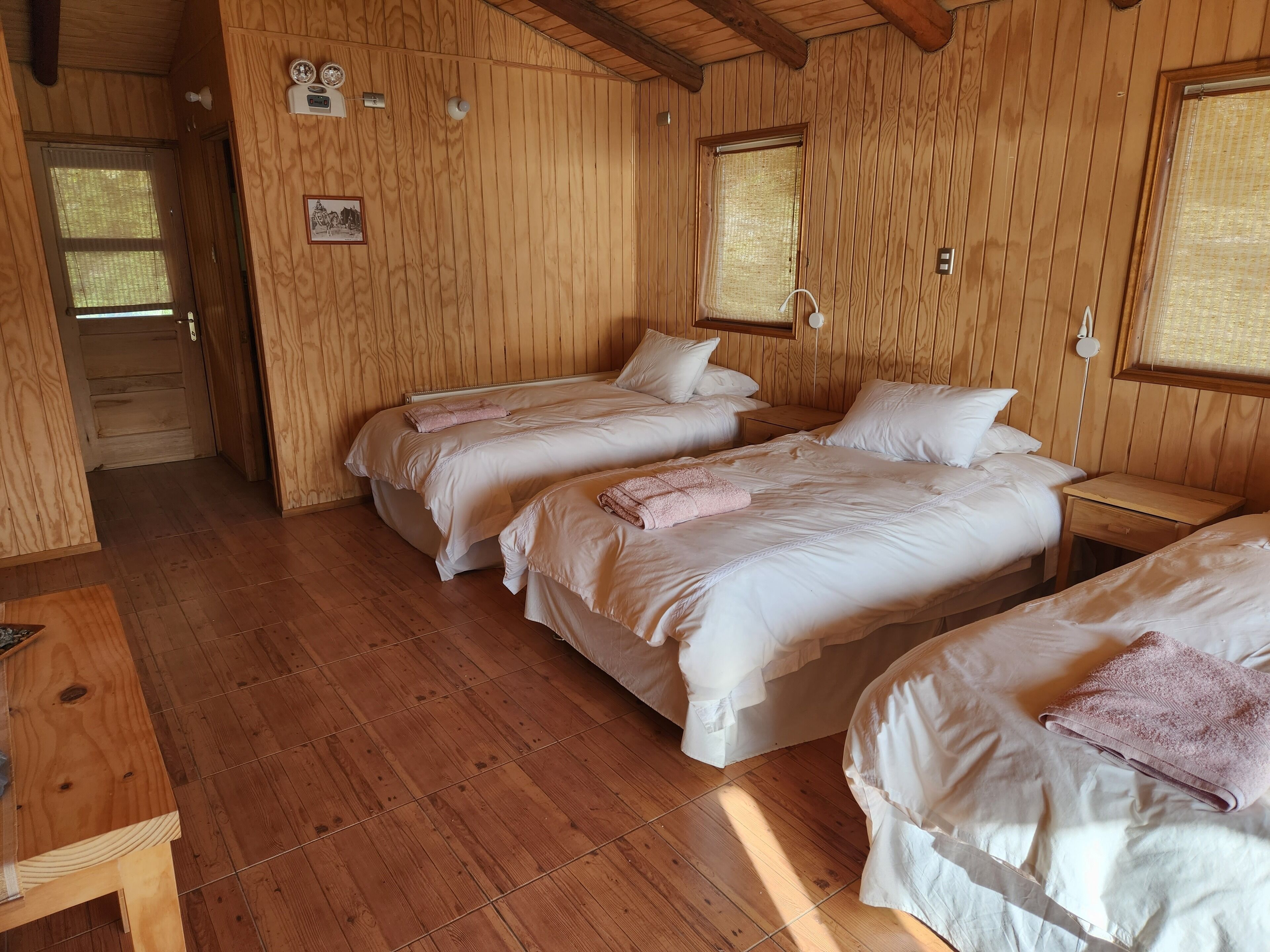 A wooden cabin with three beds, a wooden floor, and a door leading outside.