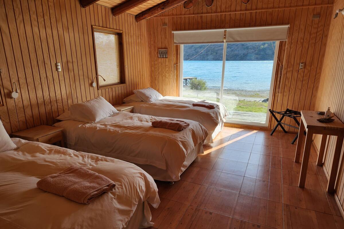 A wooden room with three beds, a small table, and a view of a lake.