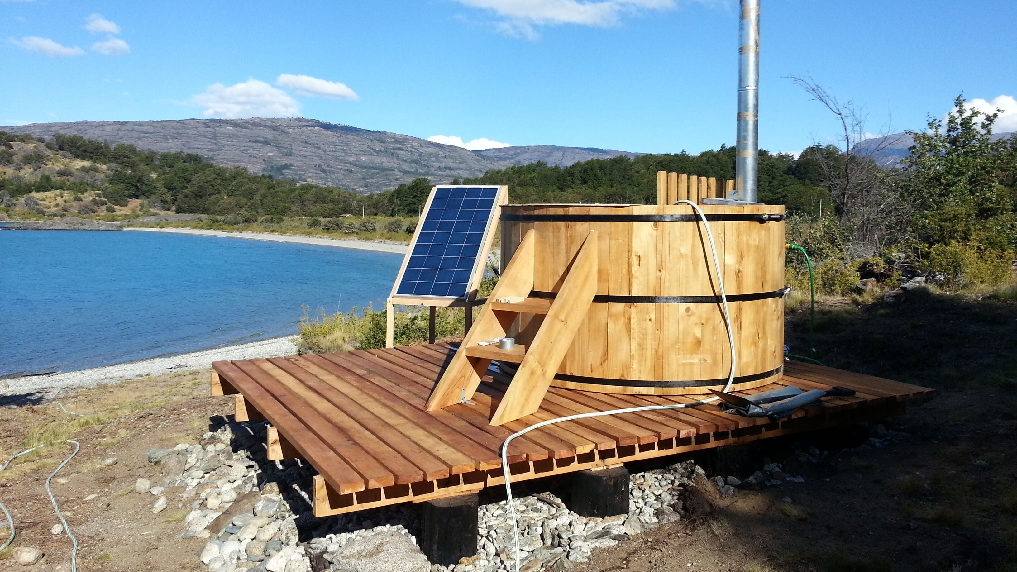 Una terraza de madera con una estructura de barril, paneles solares y una manguera.