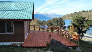 A wooden deck with a bench, a small tree, and a view of a lake and mountains. - Patagonia 47g (Chile Chico)