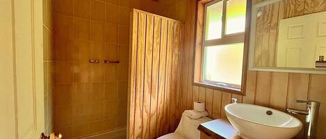 A bathroom with a wooden interior, a white toilet, a wooden vanity with a white sink, and a shower with a wooden door.