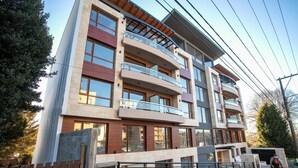 A multi-story residential building with balconies, a gated entrance, and a paved driveway. - BELGRANO SUITE (San Carlos de Bariloche)