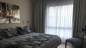 A bedroom with a large bed, a chair, a painting on the wall, and a window with curtains. - BELGRANO SUITE (San Carlos de Bariloche)