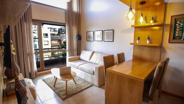 A modern living room with a sofa, a wooden dining table, and a laptop on a rug. - BELGRANO SUITE (San Carlos de Bariloche)