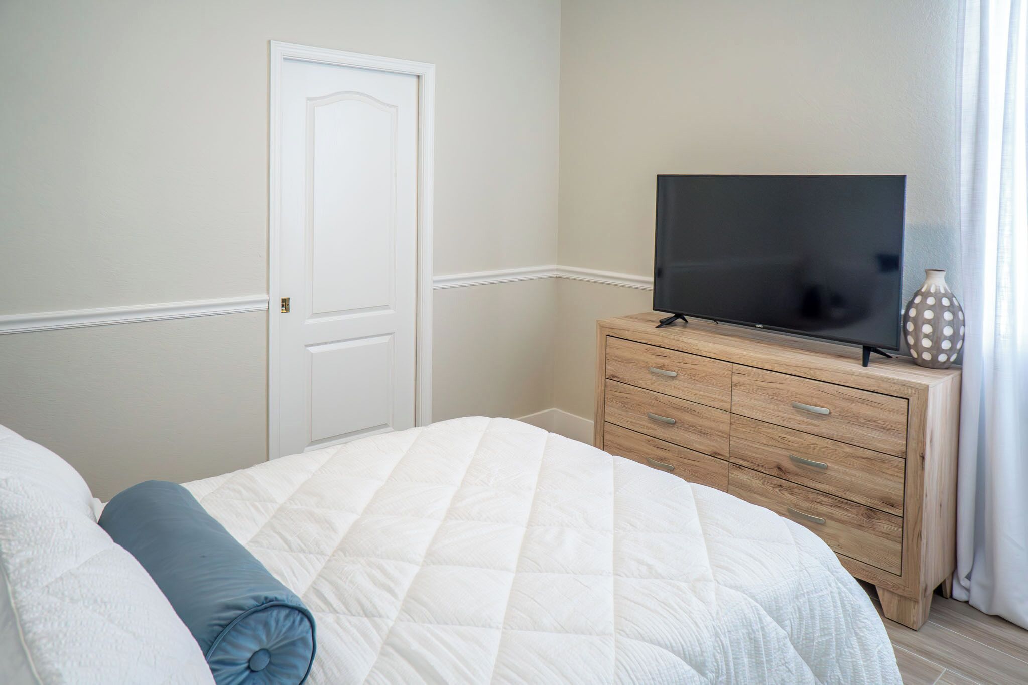 Quarto com cama, penteadeira e televisão, e uma porta.