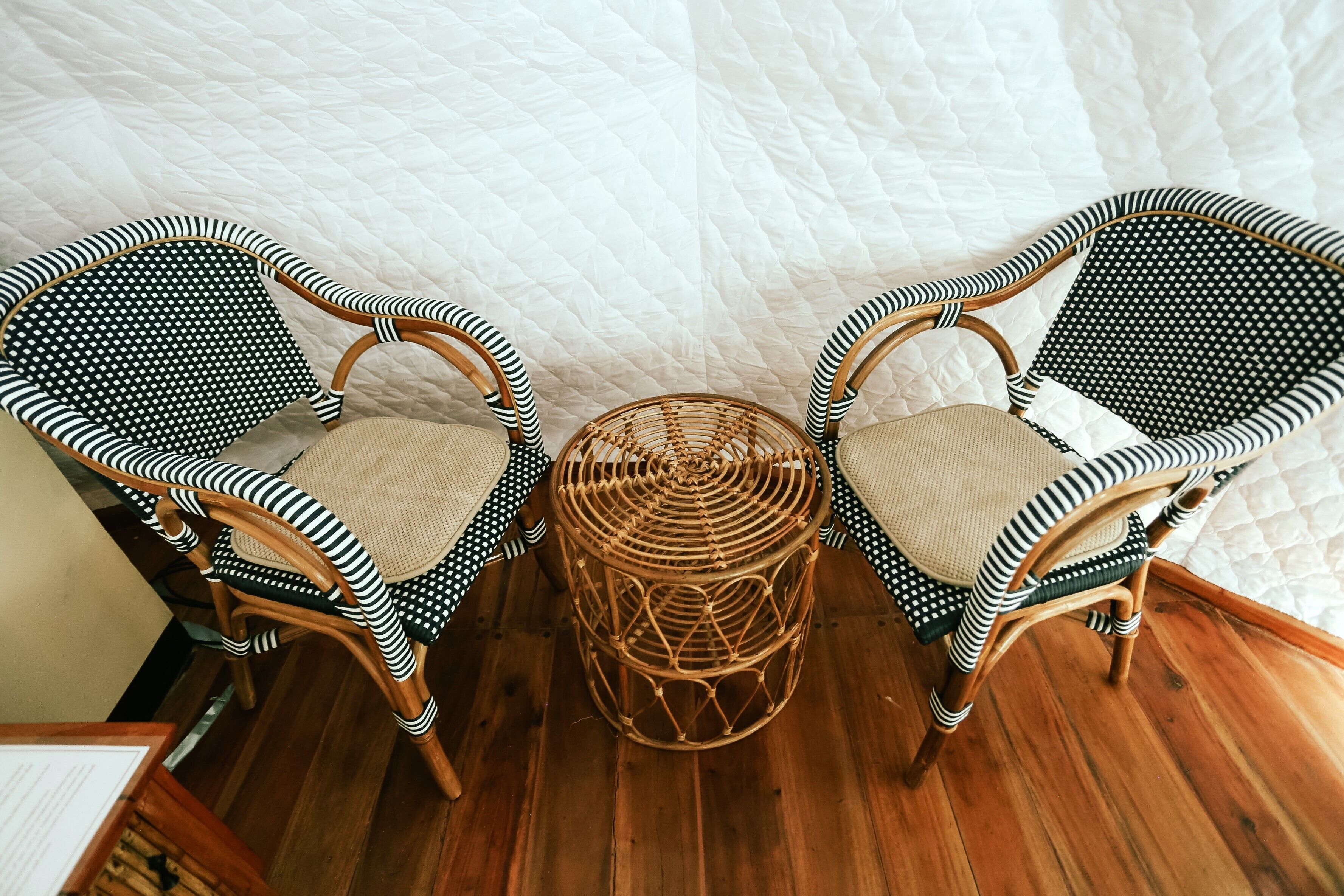 Two wicker chairs with black and white striped upholstery, a woven stool, and a wooden floor.