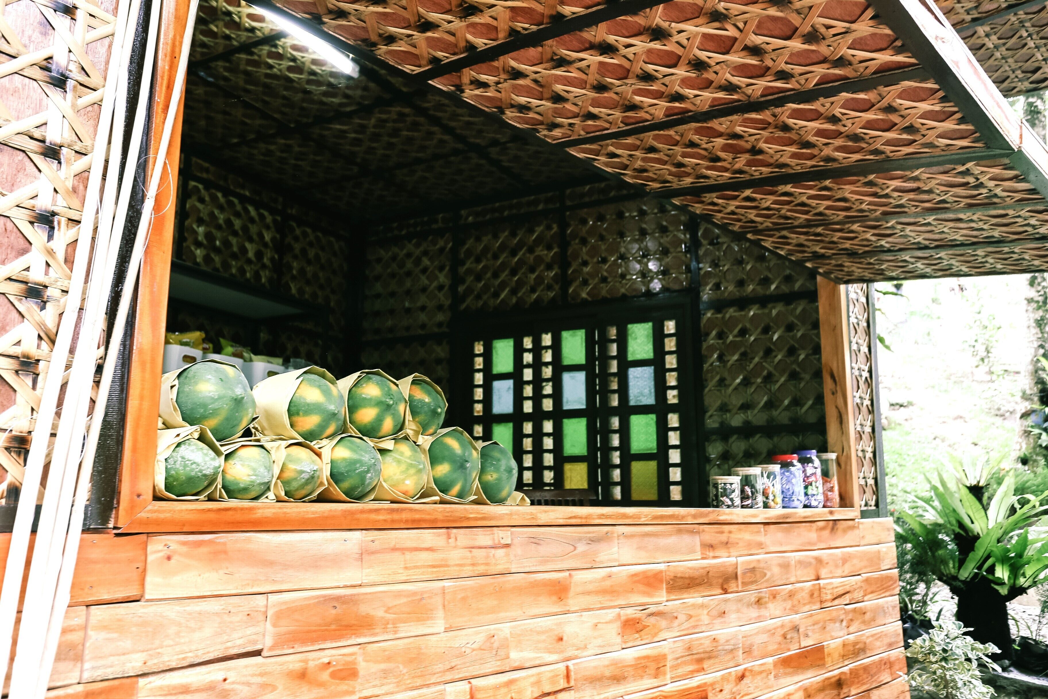 A wooden structure with a woven ceiling, a display of green fruits, and a window with a grid pattern.