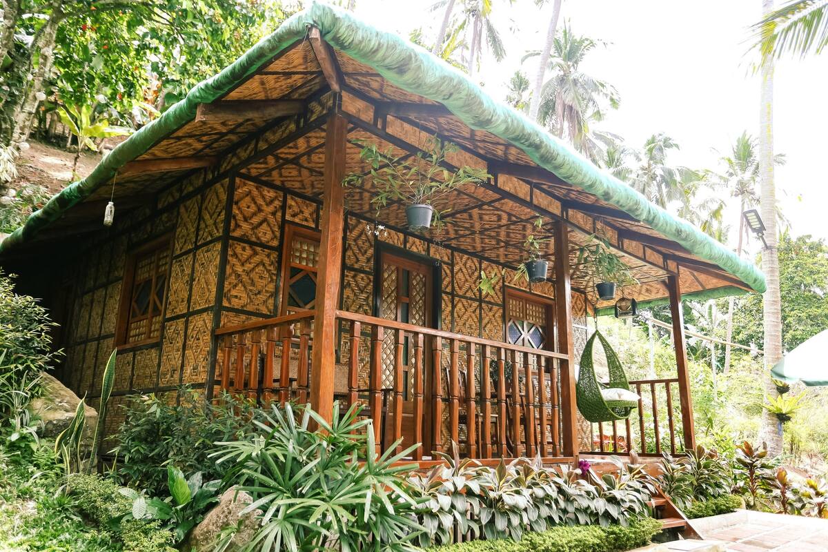 A traditional wooden structure with a thatched roof, surrounded by lush tropical vegetation.