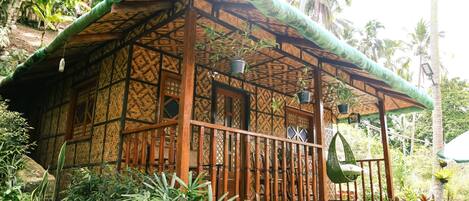 A traditional wooden structure with a thatched roof, surrounded by lush tropical vegetation.