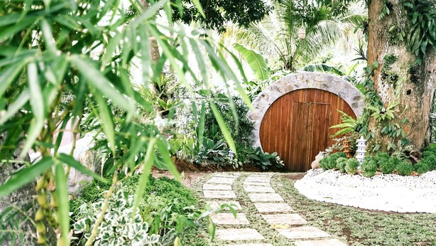 A garden pathway leading to a wooden door with a stone archway, surrounded by lush greenery and a small pagoda. - Shepherd's Ridge Mountain Resort (Mabitac)
