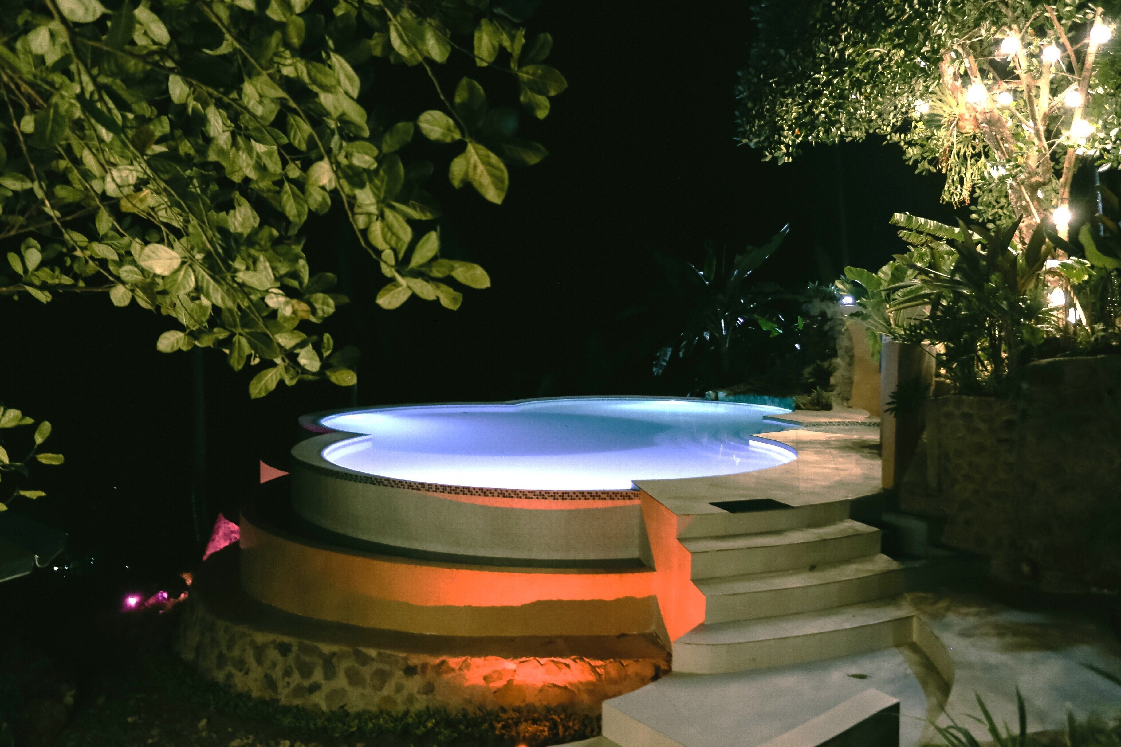 A hot tub with a tiered design, surrounded by stone steps and greenery.