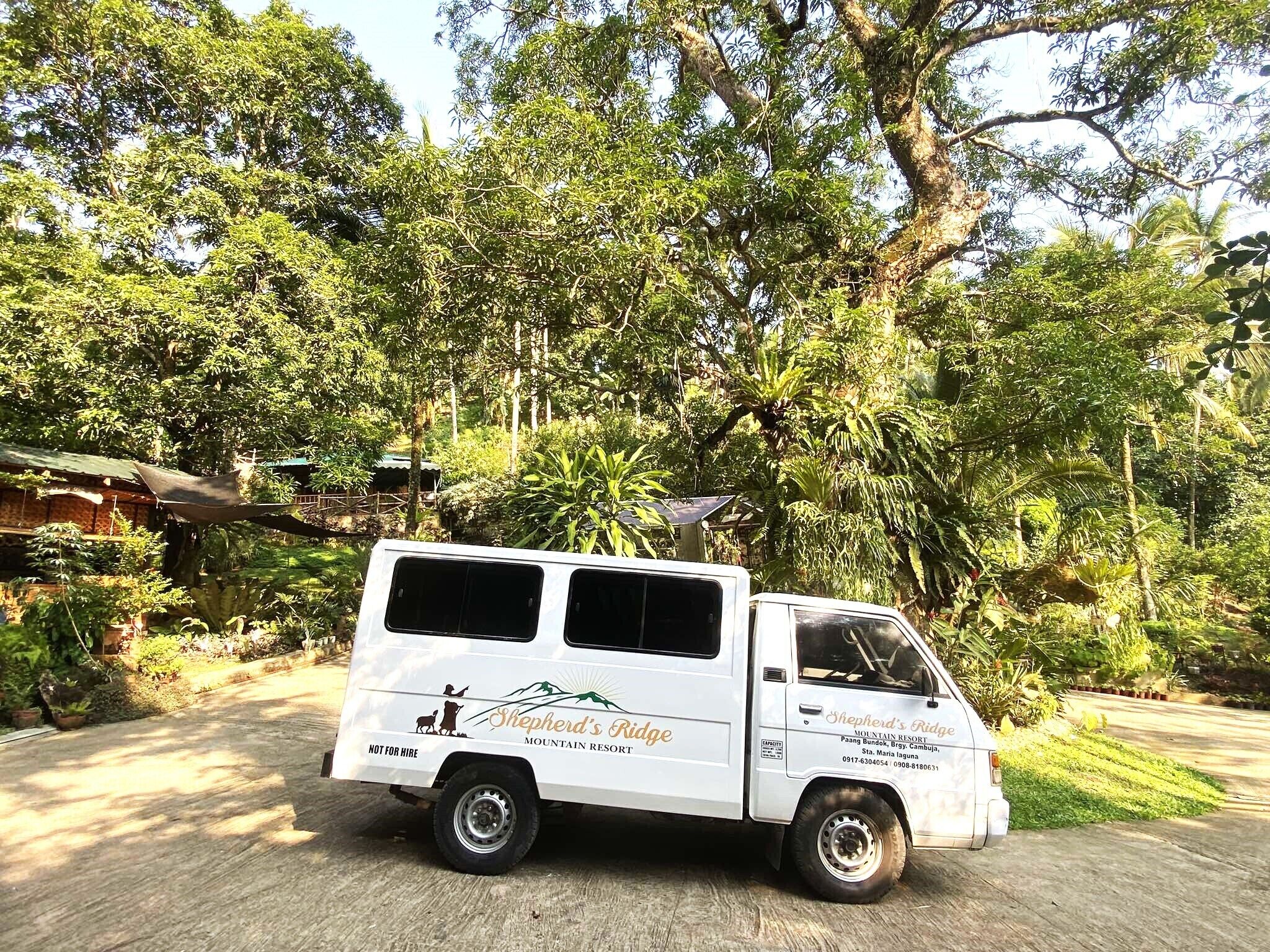 A white van with "Shepherd's Ridge" and "Mountains Resort" branding parked in a lush, green environment.