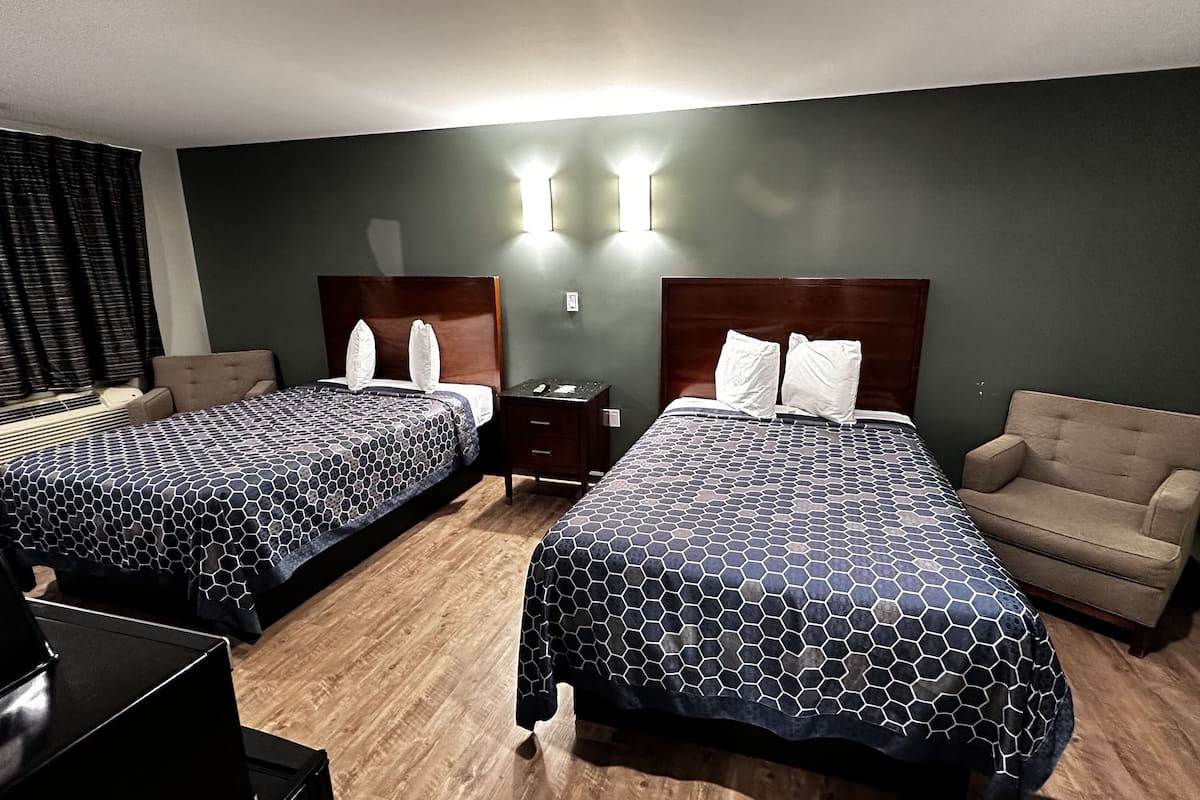A hotel room with two beds, a desk, a chair, and a nightstand.