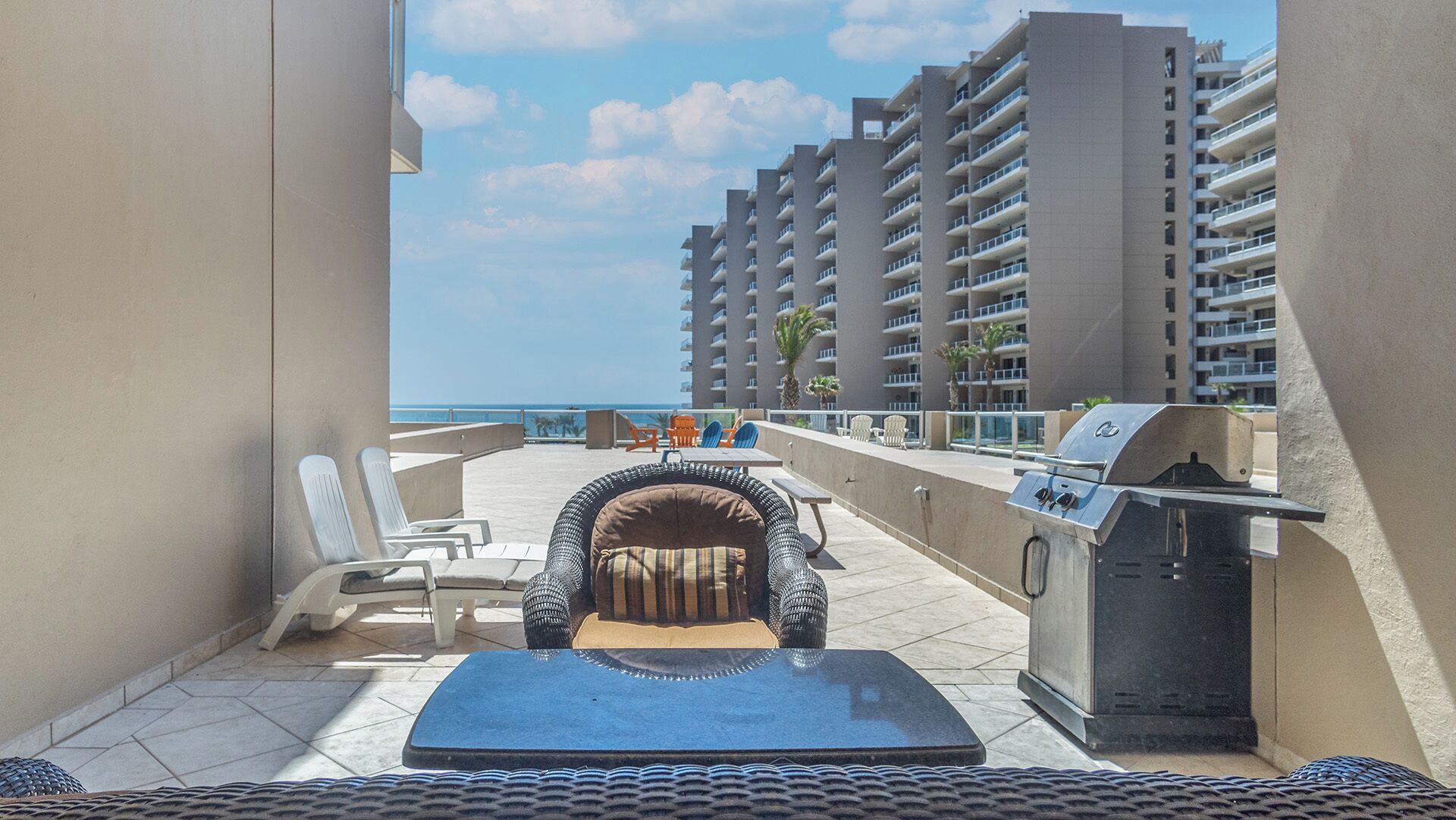 Een balkon met een barbecue, lounge stoelen en uitzicht op de oceaan en hoge gebouwen.