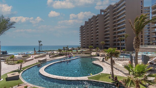 Un resort con una gran piscina, palmeras y vistas al océano.