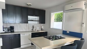 Una cocina moderna con armarios oscuros, encimera blanca, lavavajillas integrado, cocina a gas y una ventana que proporciona luz natural.