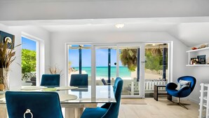 Una sala de estar moderna con una mesa de vidrio y sillas azules, una chimenea blanca y vista a la playa.
