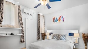 Un dormitorio con cama, unidad de aire acondicionado, ventilador de techo y una obra de arte en la pared.