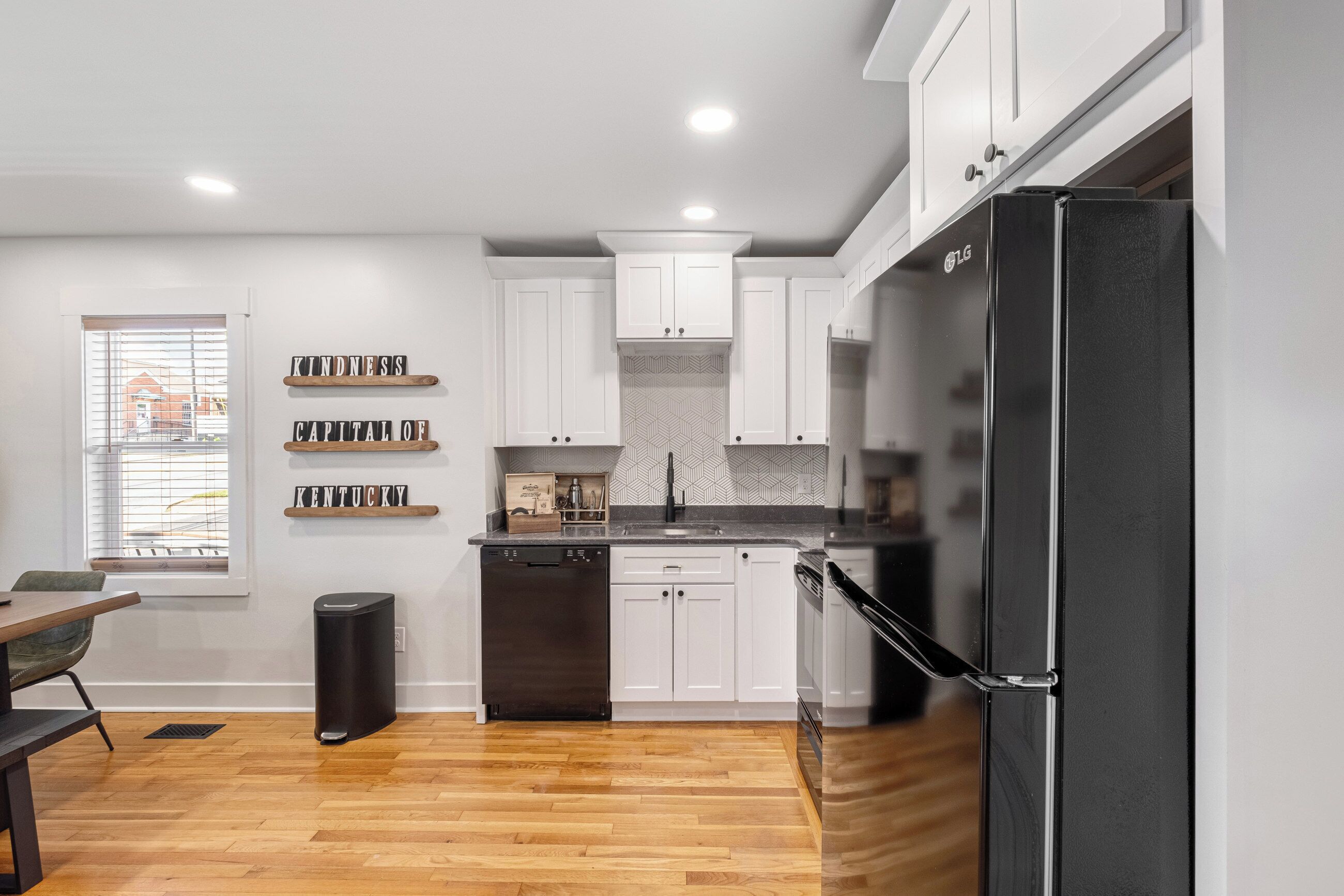A modern kitchen with white cabinets, a black refrigerator, and a wooden floor.