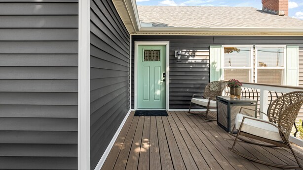 A wooden deck with a green door, wicker chairs, and a small table.