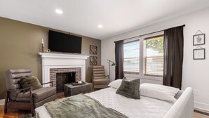A bedroom with a large bed, a fireplace, a TV, and a window with curtains.