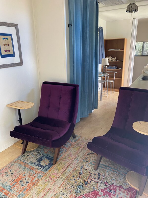 A room with two purple armchairs, a small wooden table, a colorful rug, a framed picture on the wall, and a glimpse of a dining area with a table and chairs. - Secret Garden in gorgeous Sedona with AC, WiFi (Sedona)