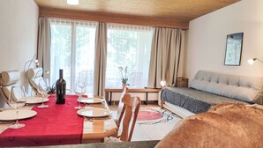 A cozy room with a dining table set for two, a bed with a grey duvet, and a window with curtains.