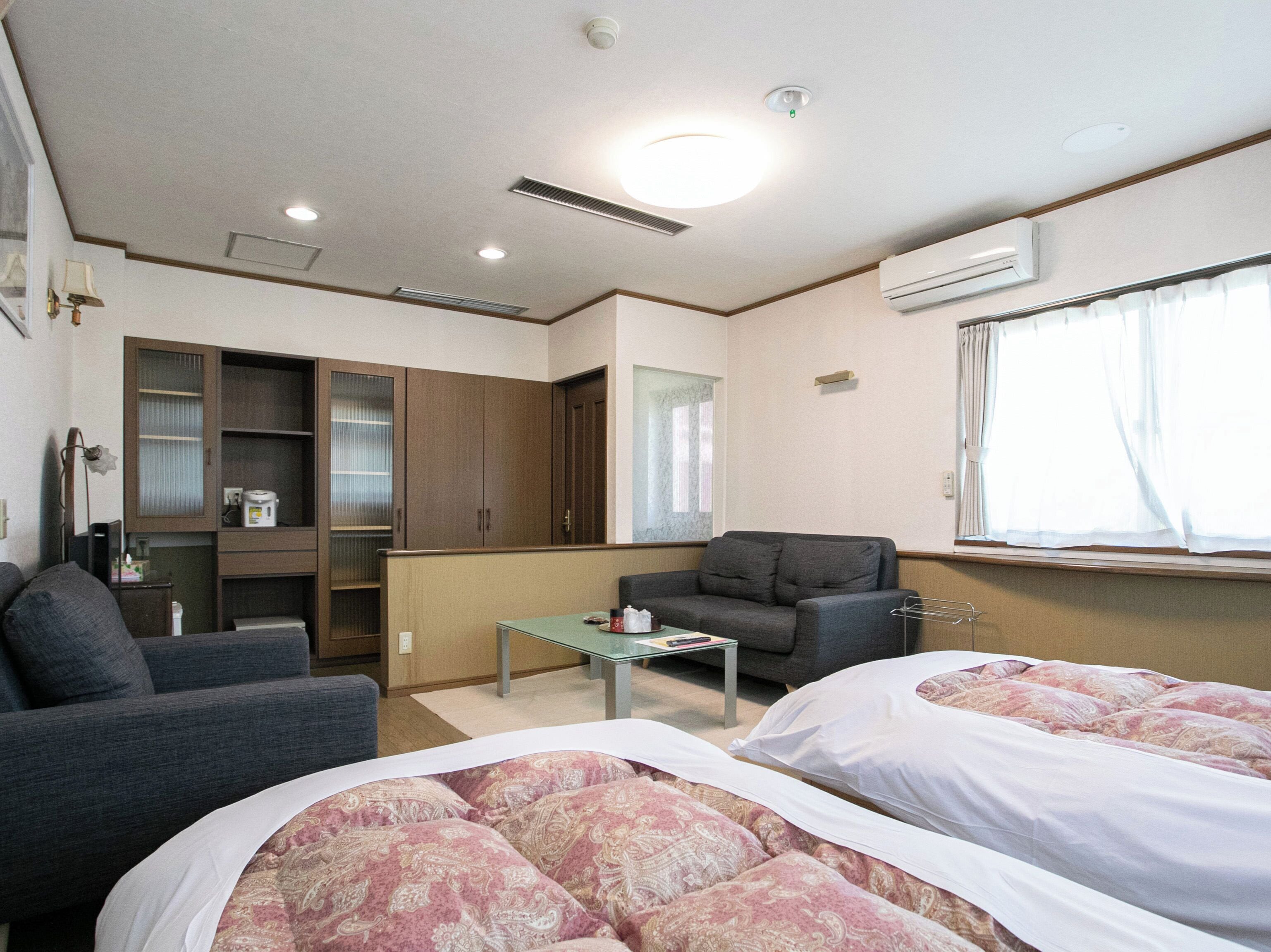 A hotel room with two beds, a sofa, a small table, and a cabinet.
