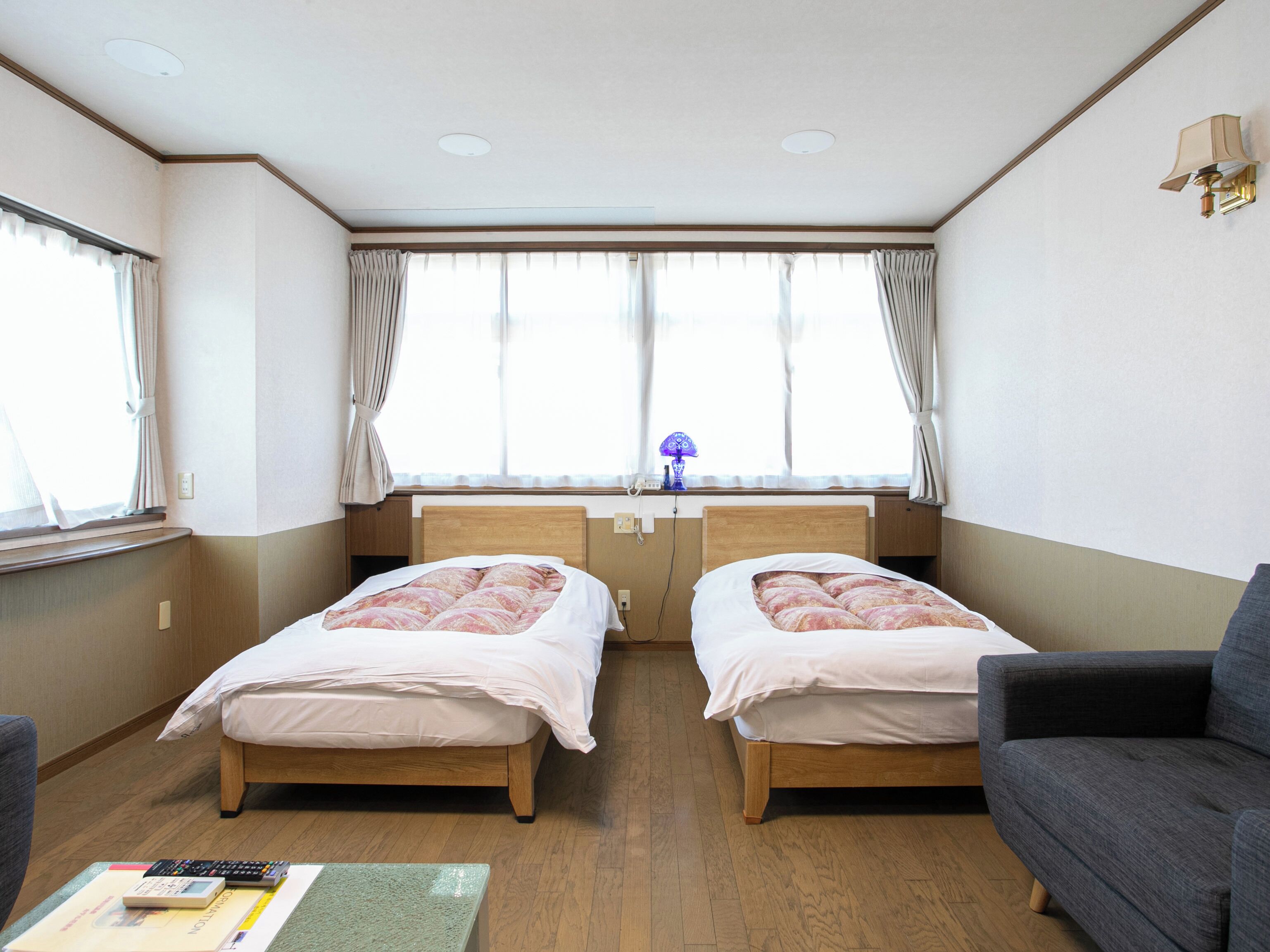Une chambre avec deux lits, un bureau, une chaise et une fenêtre avec des rideaux.
