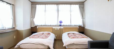 Une chambre avec deux lits, un bureau, une chaise et une fenêtre avec des rideaux.