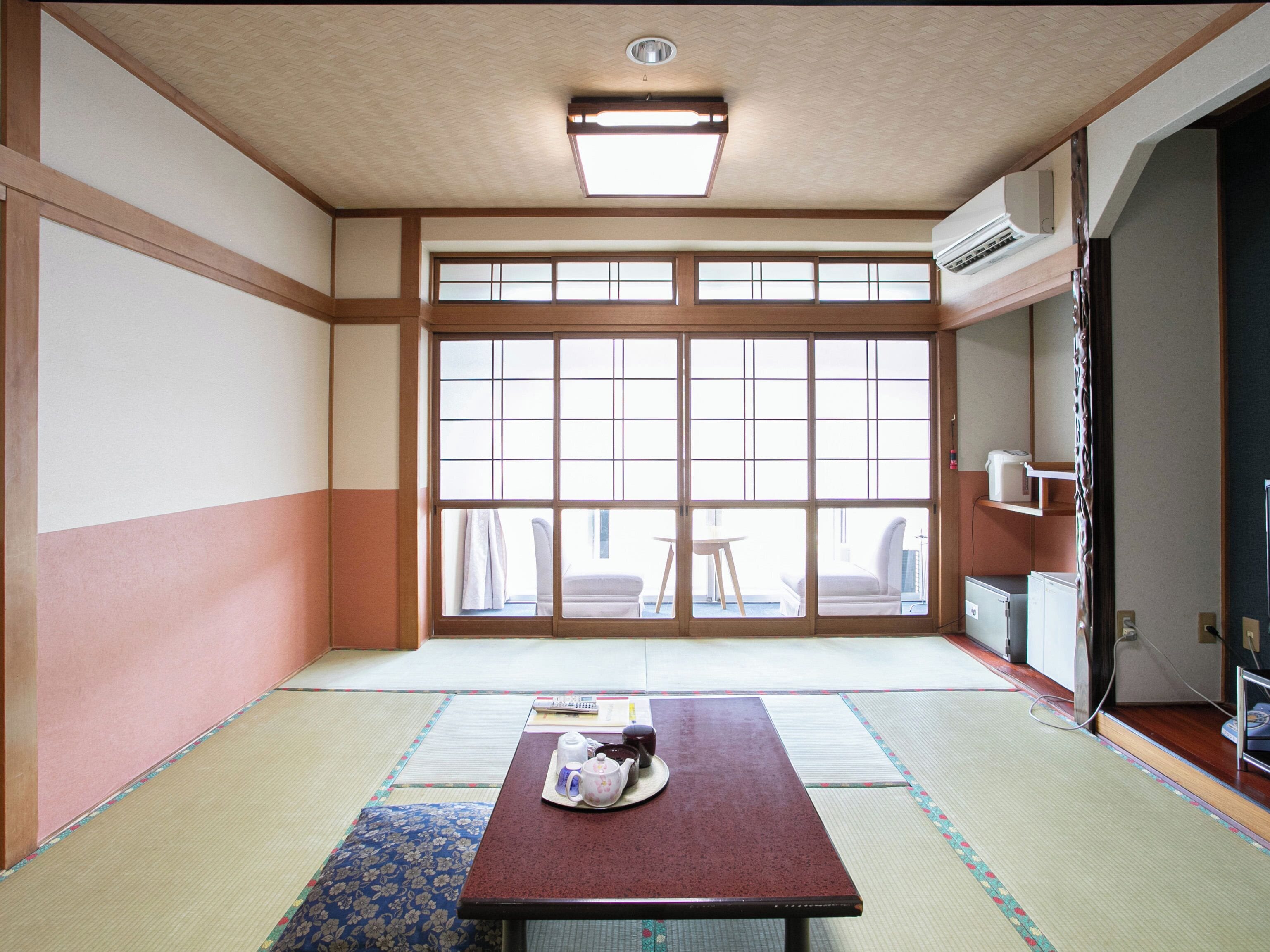Una habitación japonesa tradicional con suelo de tatami, una mesa baja con juego de té y un ventanal con puertas correderas.