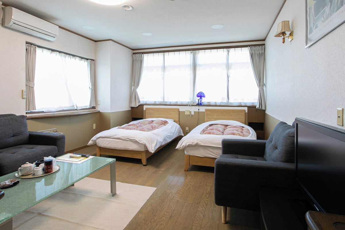 Une chambre d’hôtel avec deux lits simples, un canapé, une petite table avec une théière et des tasses, et un téléviseur.