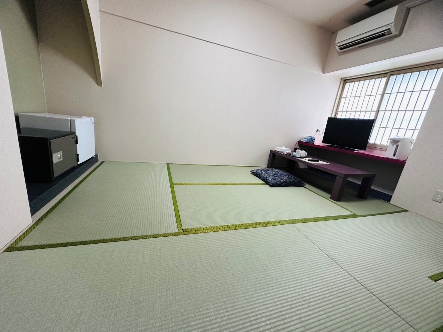 Una habitación con esteras de tatami, un escritorio con una computadora, un televisor y un calentador pequeño.