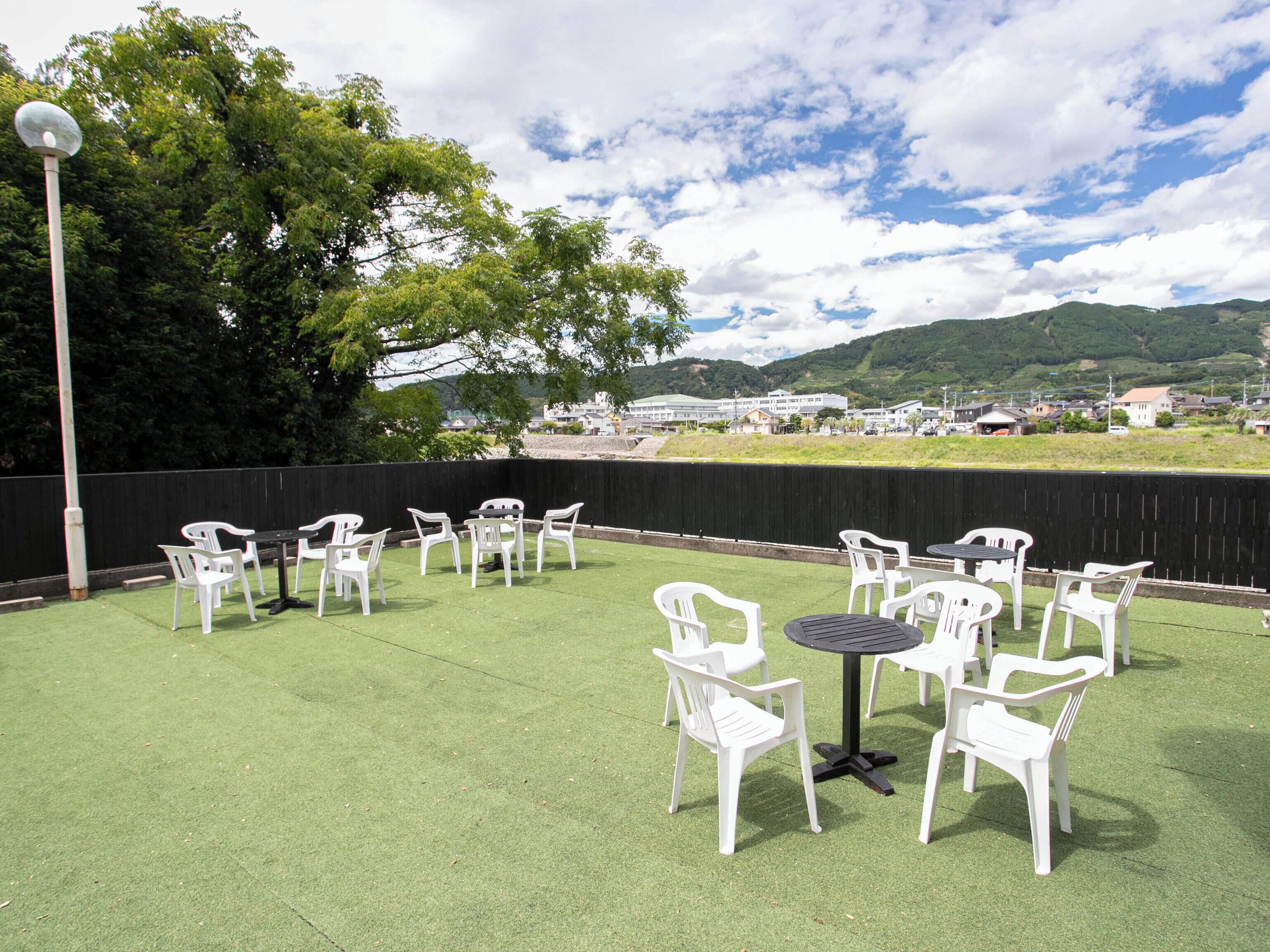An outdoor patio with white plastic chairs and tables, a black lamp post, and a view of a town and hills in the background.