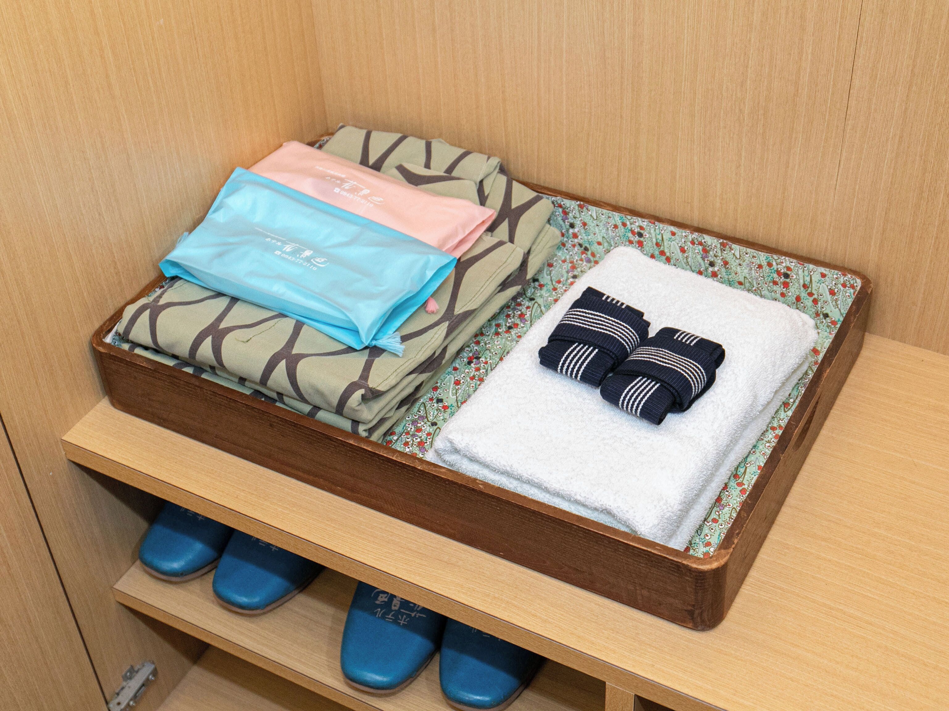 A neatly organized storage area with folded towels, a pair of slippers, and a folded garment.