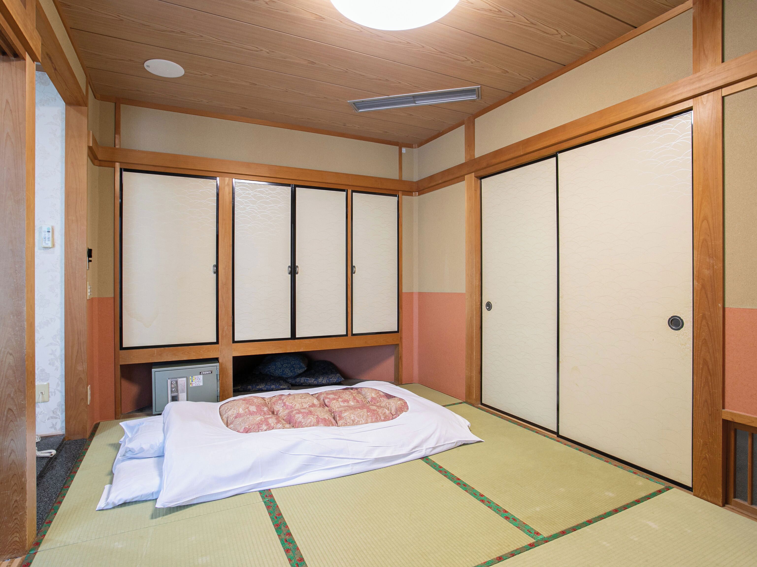 Una habitación japonesa tradicional con suelo de tatami, una cama con ropa blanca y puertas correderas.