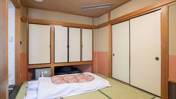Una habitación japonesa tradicional con suelo de tatami, una cama con ropa blanca y puertas correderas.