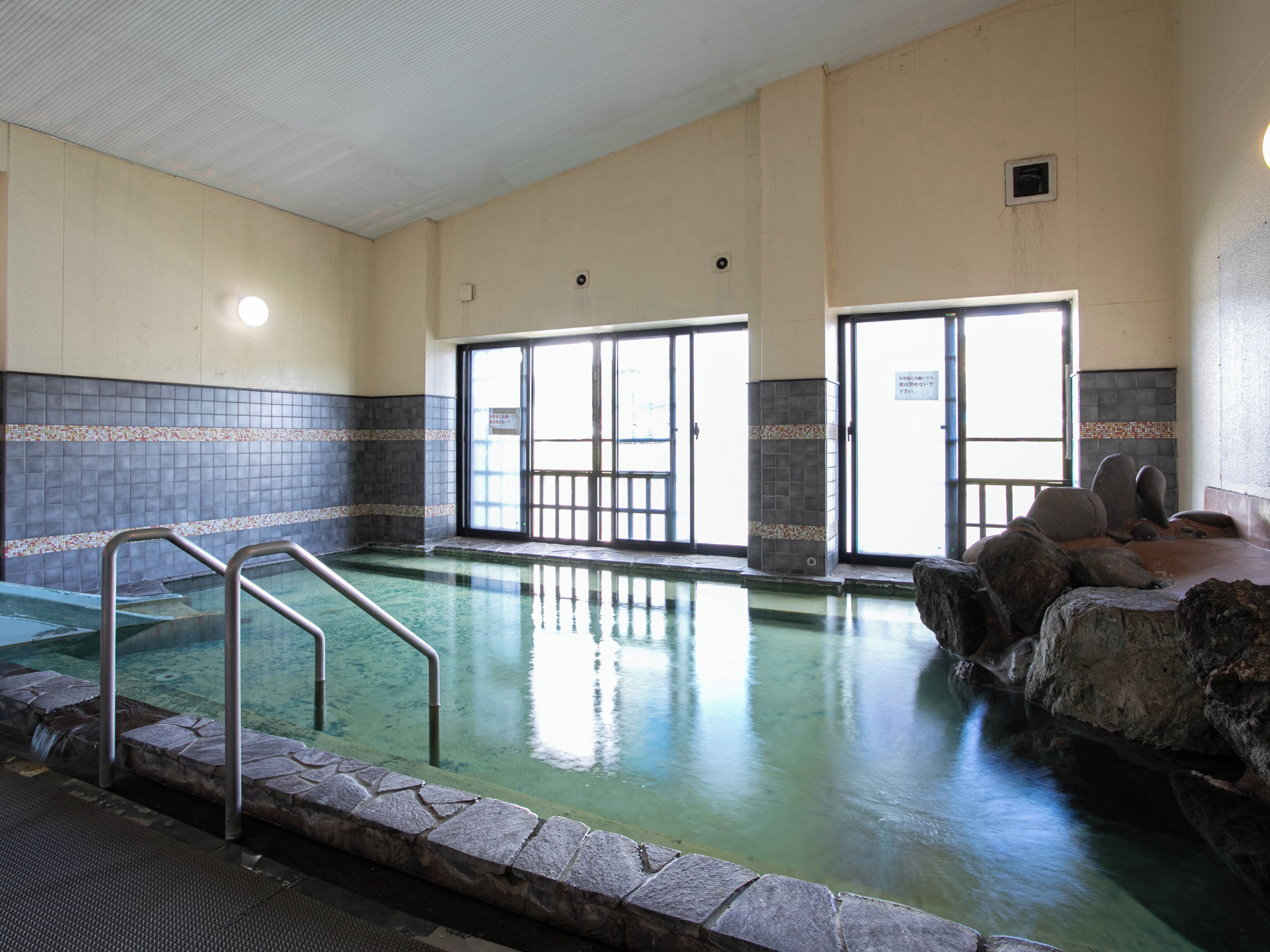 An indoor swimming pool with clear water, stone steps leading into the pool, and tiled walls.