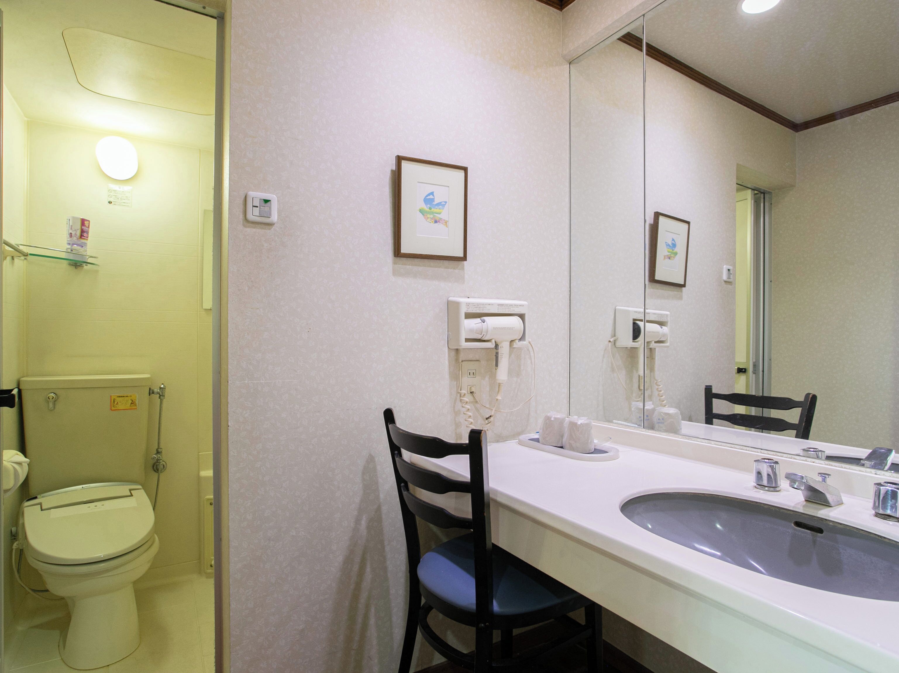 Un baño con inodoro, lavamanos, silla y espejo.