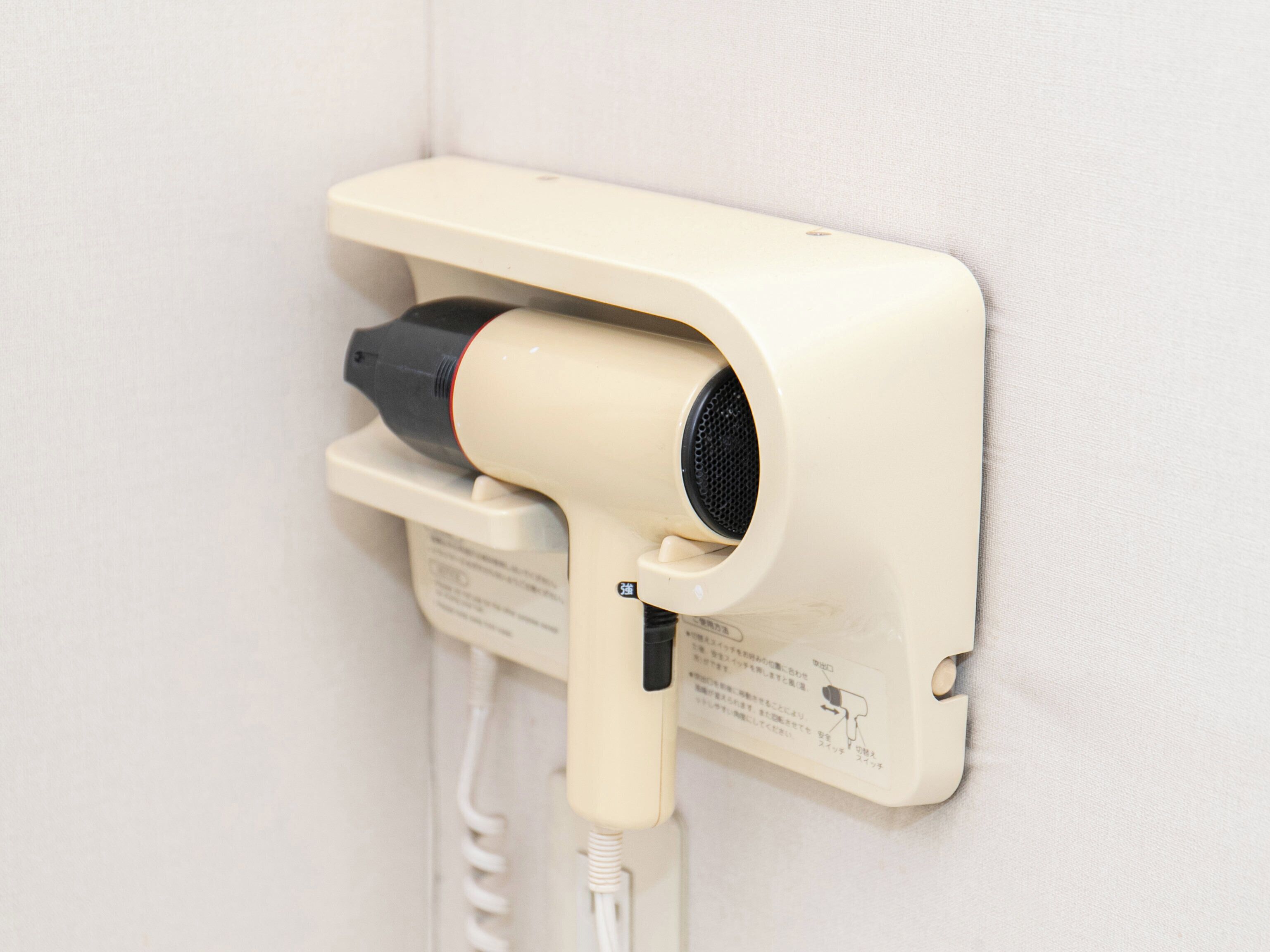 A hairdryer mounted on a wall with a power cord plugged in.