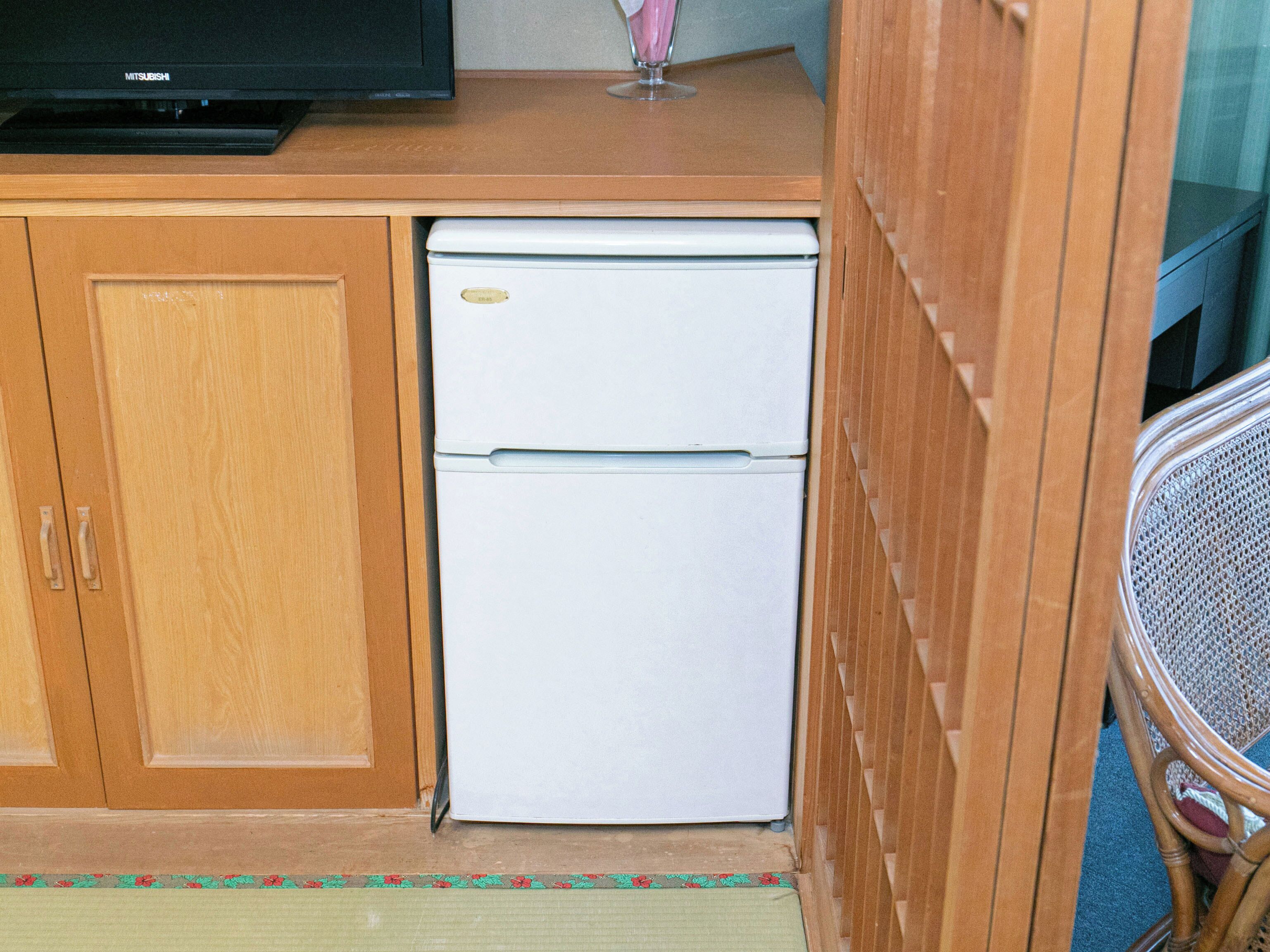 A compact kitchenette with a white refrigerator, wooden cabinets, and a small television on top.