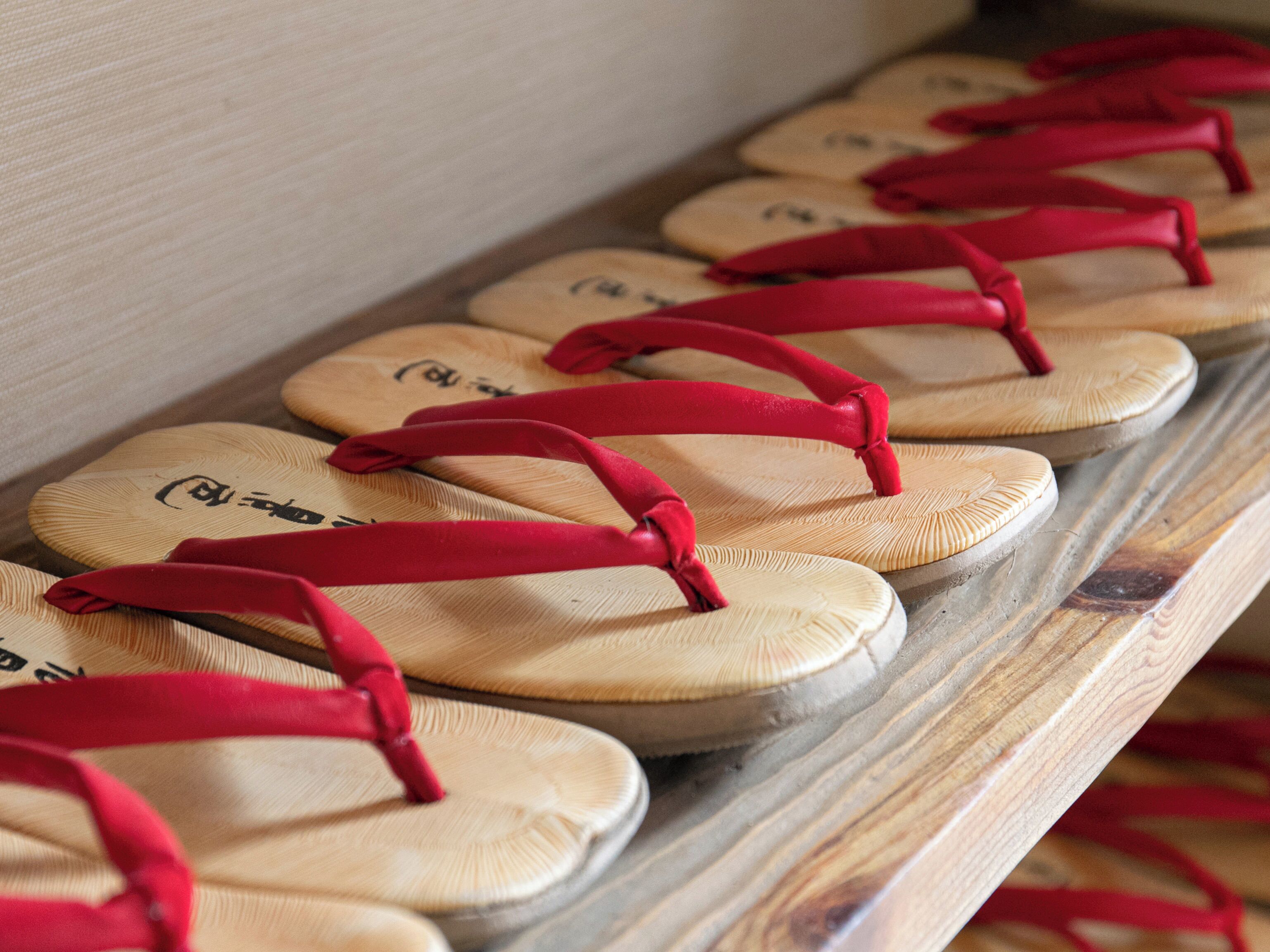 A row of wooden flip-flops with red straps on a shelf.