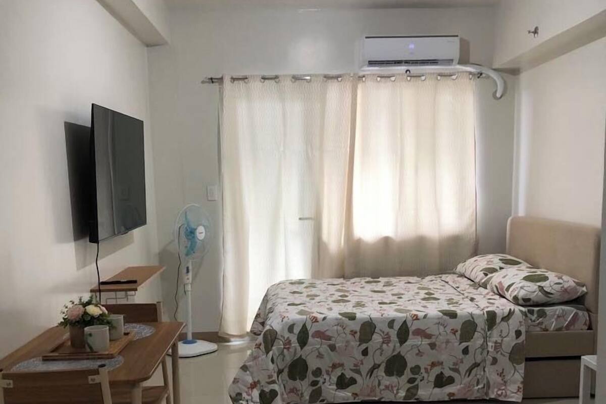 Quarto com cama, escrivaninha com cadeira, televisão na parede e ar condicionado.
