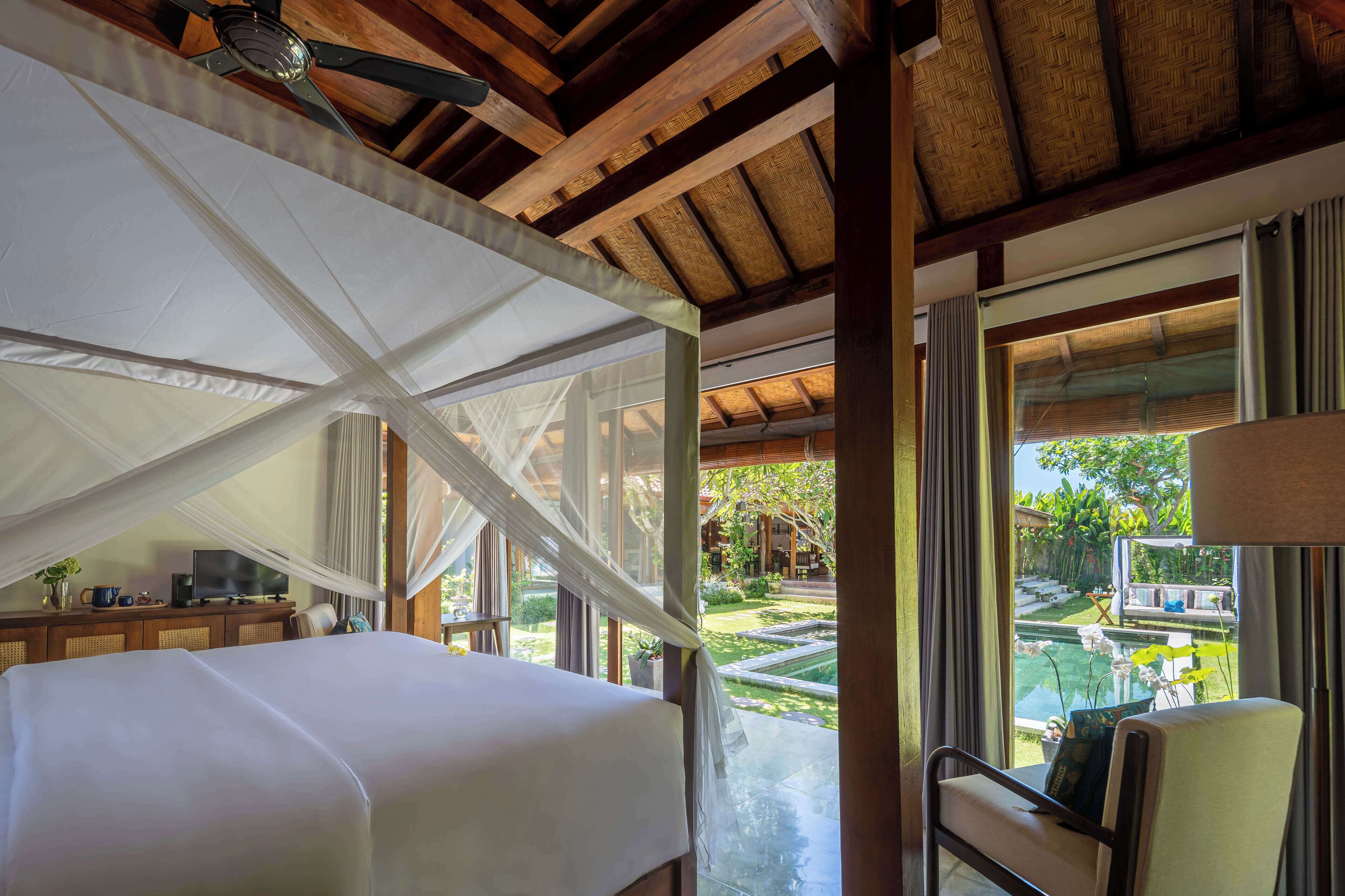 A bedroom with a bed, a television, and a view of a swimming pool and garden.