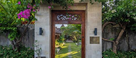 Una entrada de piedra con una puerta de madera, rodeada de abundante follaje y plantas florecientes.