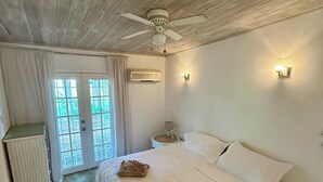 A bedroom with a large bed, a ceiling fan, a nightstand with a lamp, and a view through a glass door.