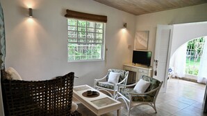 A cozy living room with wicker furniture, a television, and a large window with a view of greenery.