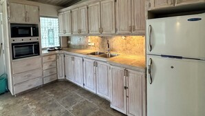 A kitchen with light wooden cabinets, a double sink, a white refrigerator, and a microwave.