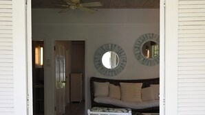 A room with a bed, two chairs, a table, a ceiling fan, and two wall mirrors.